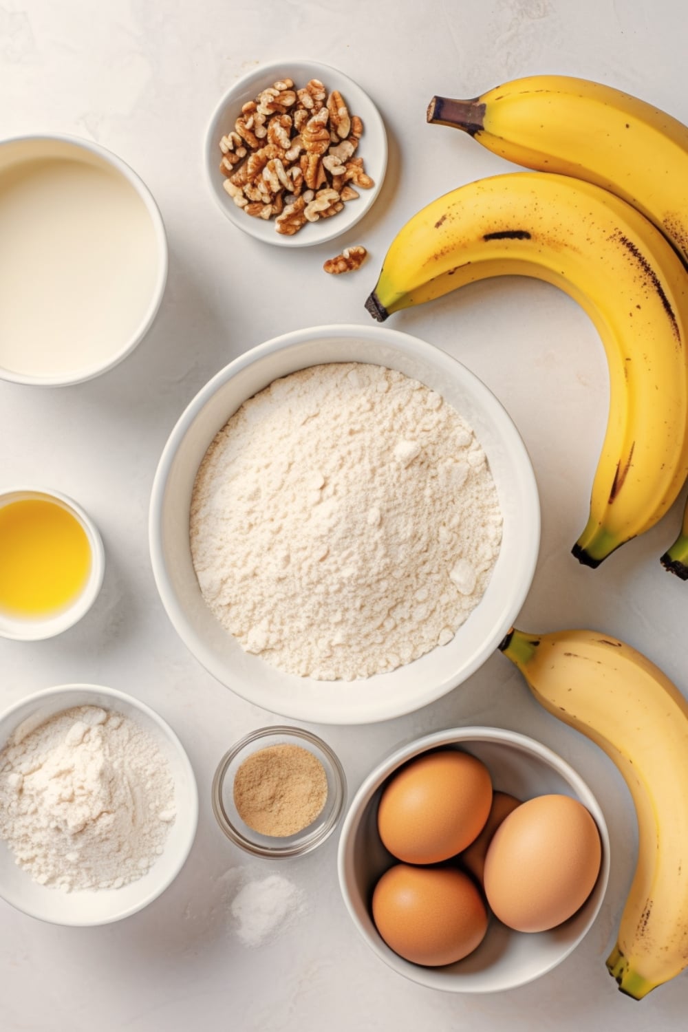 Banana bread ingredients: Butter, sugar, eggs, vaniila extract, lemon juice, flour, baking soda, salt, sour cream, chopped walnuts, ripe bananas on a white surface. 
