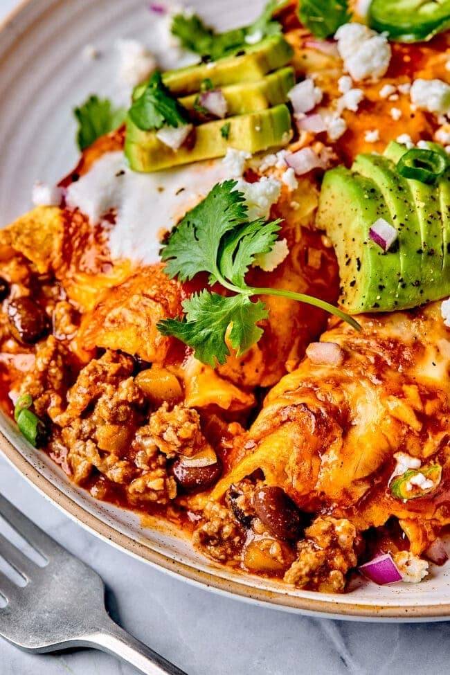 Beef enchiladas served on a plate topped with sliced avocado and cheese. 