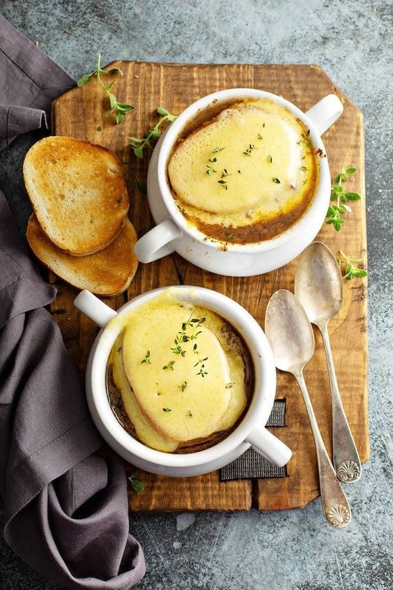 Beef and barley soup topped with melted cheese on a white mug with toasted bread. 