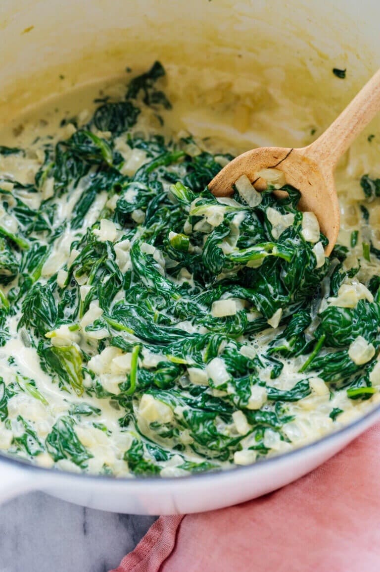 Bowl of creamed spinach mixed with a wooden spoon. 