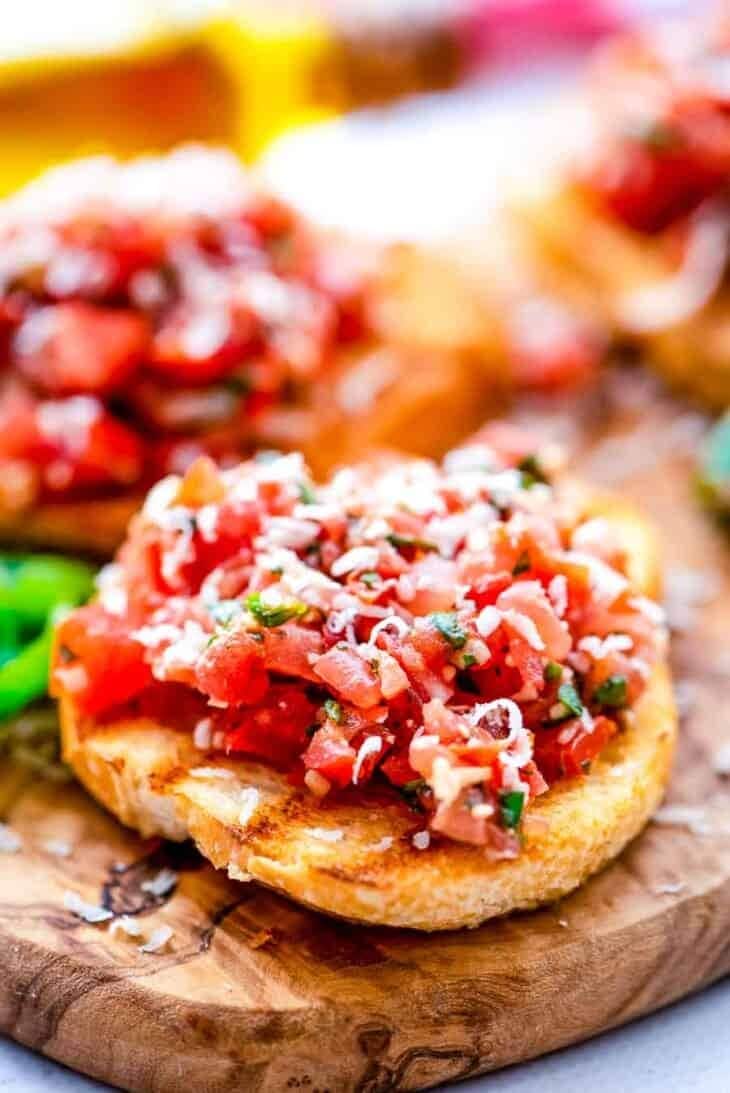Bruschetta topped with sliced tomatoes and herbs served on a wooden board.  