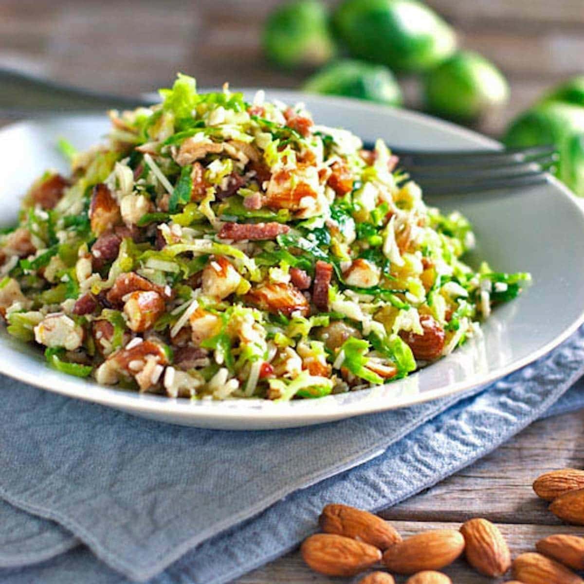 Bacon and brussels sprout salad with crumbled bacon, parmesan cheese and almonds served on a plate. 
