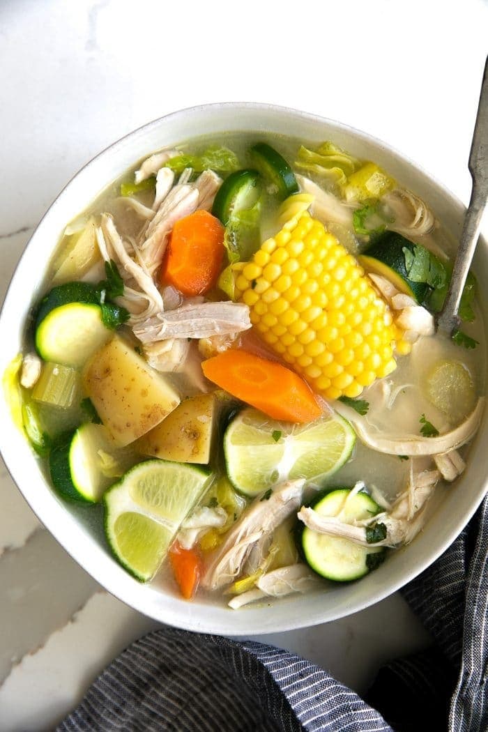 Caldo de pollo soup with vegetables, corns and chicken meat served on a white bowl. 