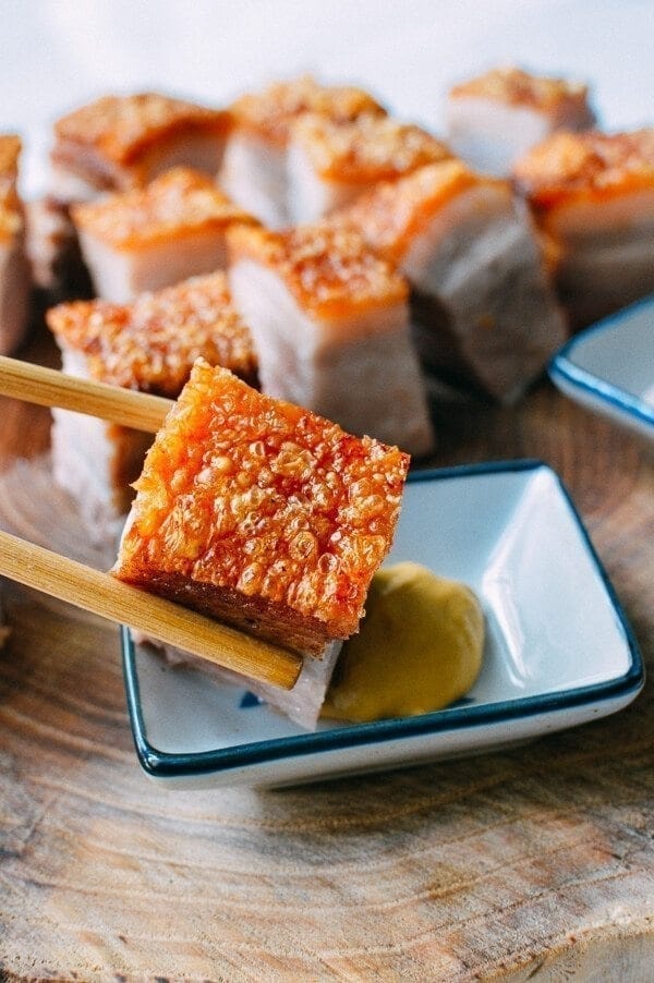 Chopsticks dipping Cantonese Roast Pork Belly on a saucer with sauce