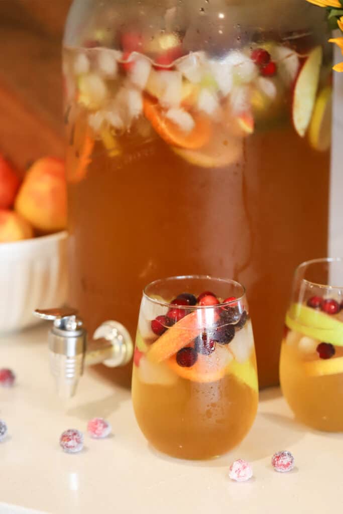 A jag of caramel apple punch served on glasses garnished with berries and lemon peel. 