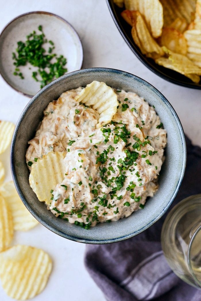 Creamy onion dip on a bowl with chips, garnished with chopped onion leaves on top.