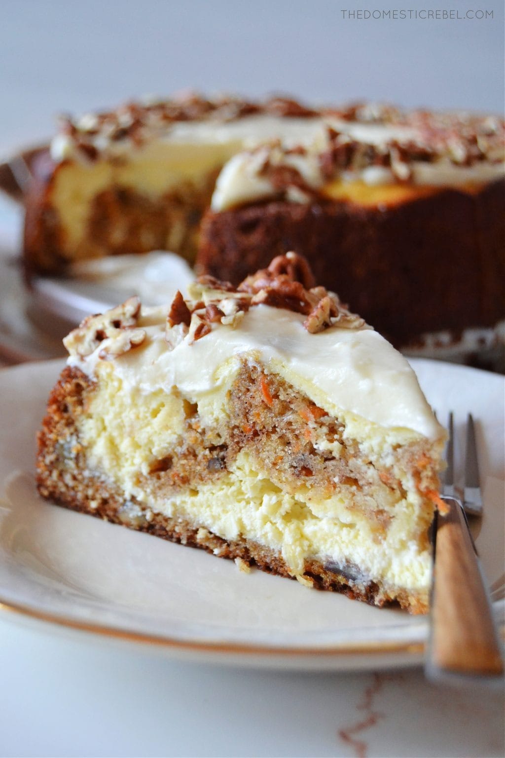 A slice of Carrot Cake Cheesecake on a saucer with chopped pecans on top