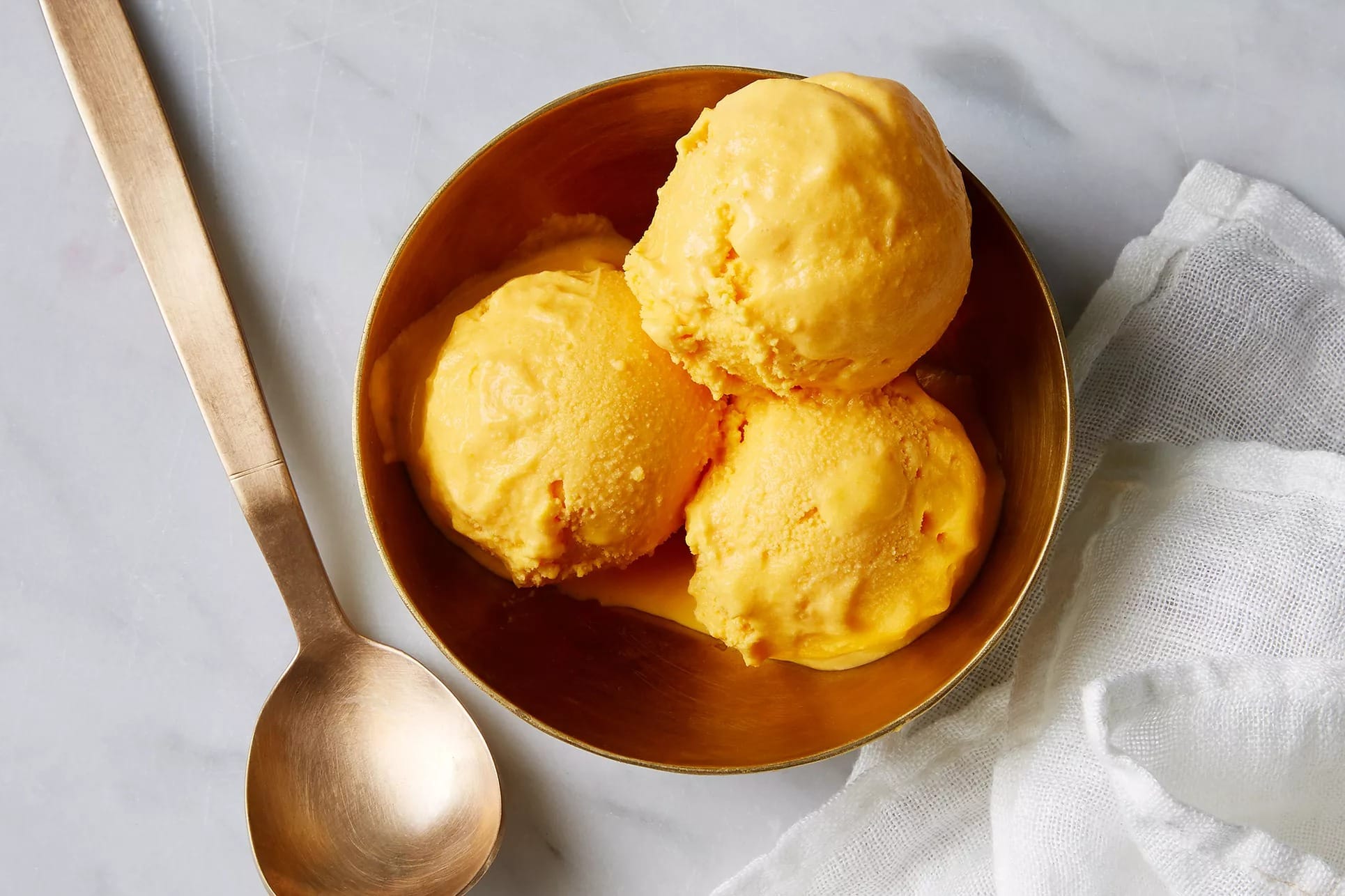Three scoops of homemade Carrot Ice Cream on a stainless bowl