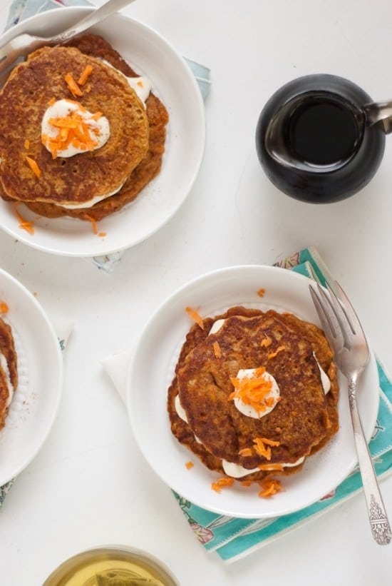 Top view of Carrot Pancakes with cream cheese on top and a bottle of vanilla syrup on the side