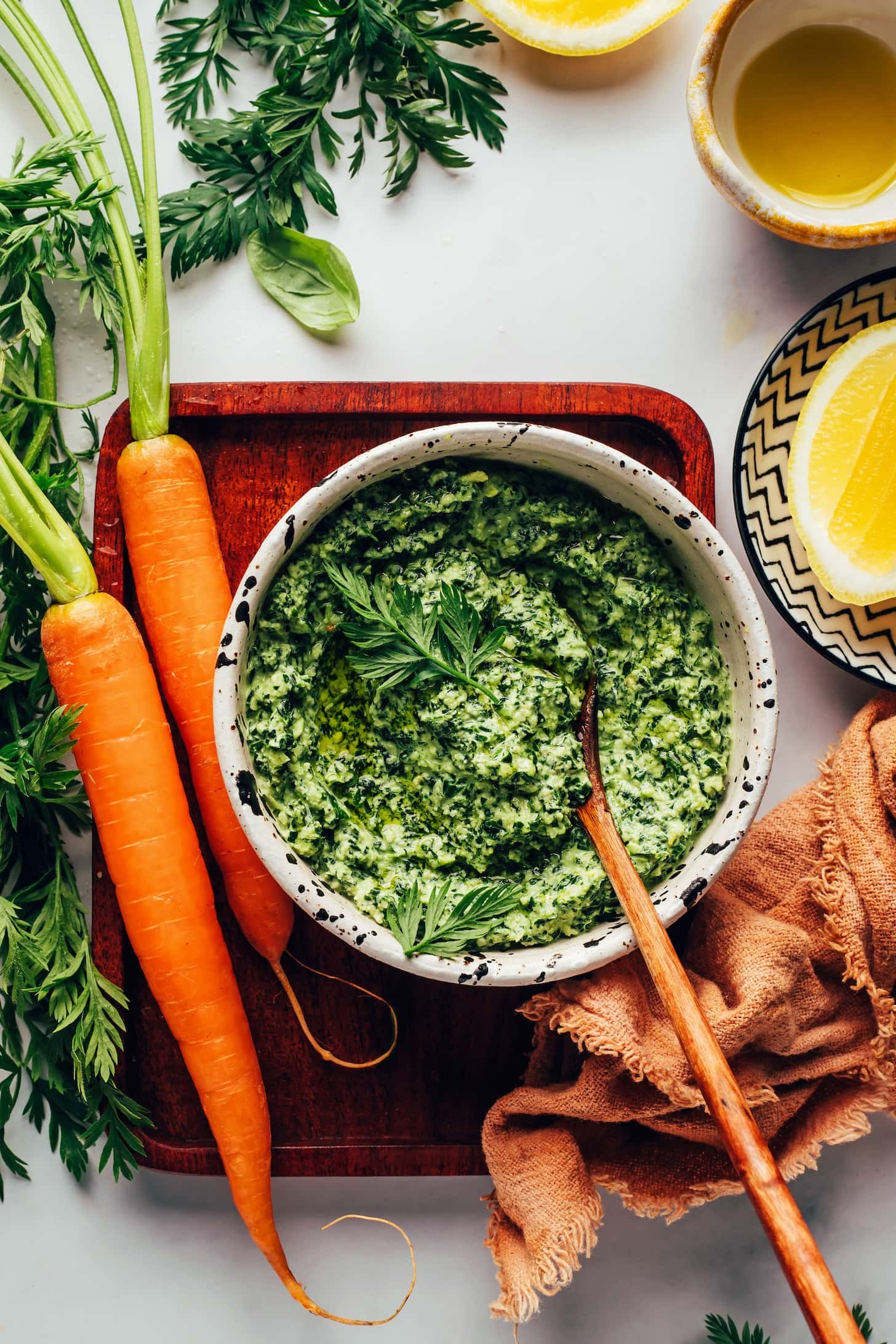 Bowl of Carrot Top Pesto with fresh carrots on a wooden tray