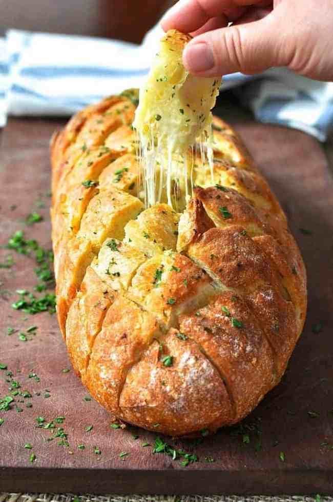 Pull apart bread made with cheese and garlic garnished with chopped parsley leaves placed on top of a wooden board. 