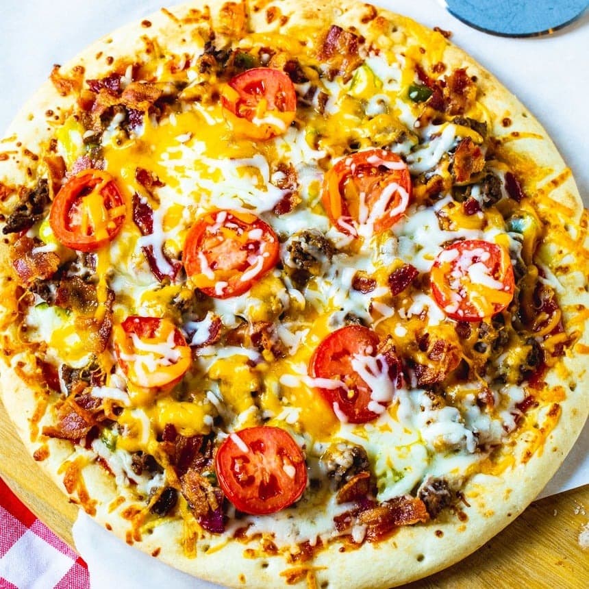 Whole cheesy cheeseburger pizza topped with tomatoes, ground beef, pickles and bacon. 