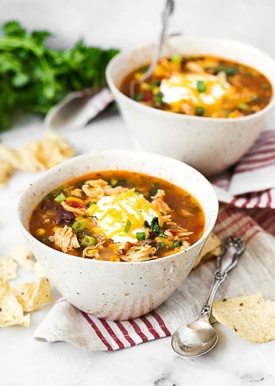 Chicken enchilada soup in bowls top with cream and grated cheese. 