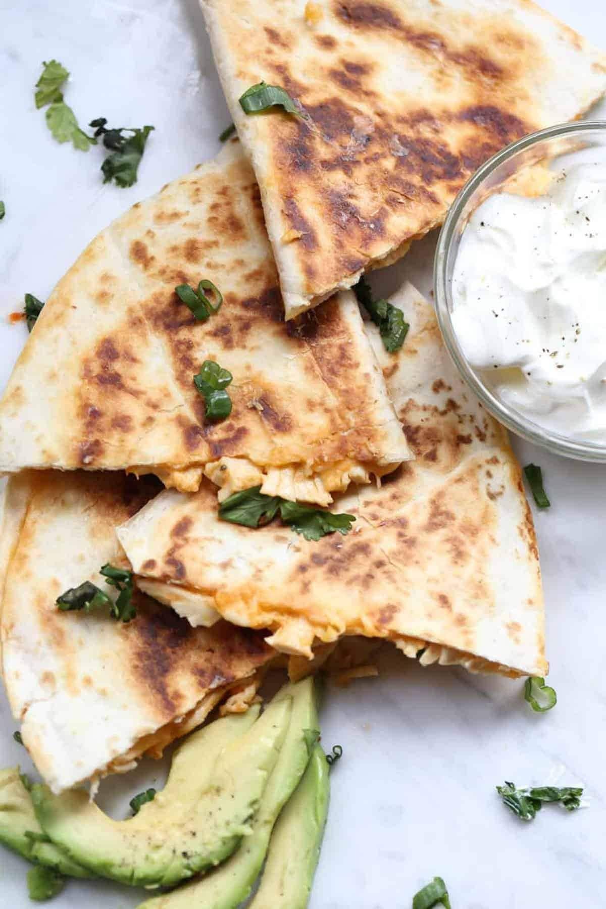 Stacks of Chicken Quesadilla with a bowl of cream 