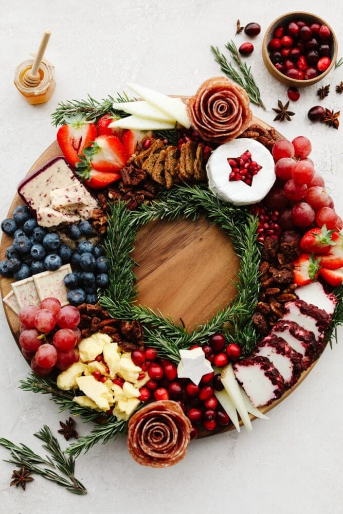 Christmas inspired charcuterie board with cheese, berries and nuts served on a round wooden board. 
