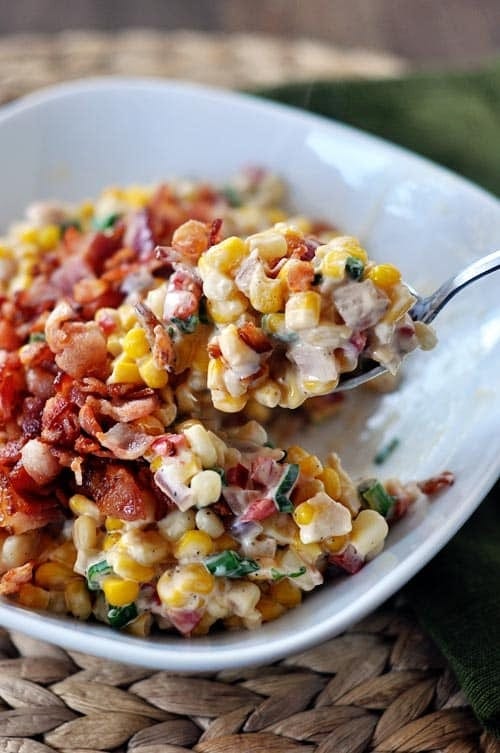 Spoon scooping creamy confetti corn salad with bacon from a bowl.  