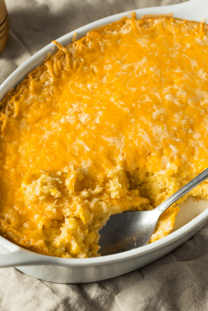 Cheesy corn casserole in a white oval dish with spoon.