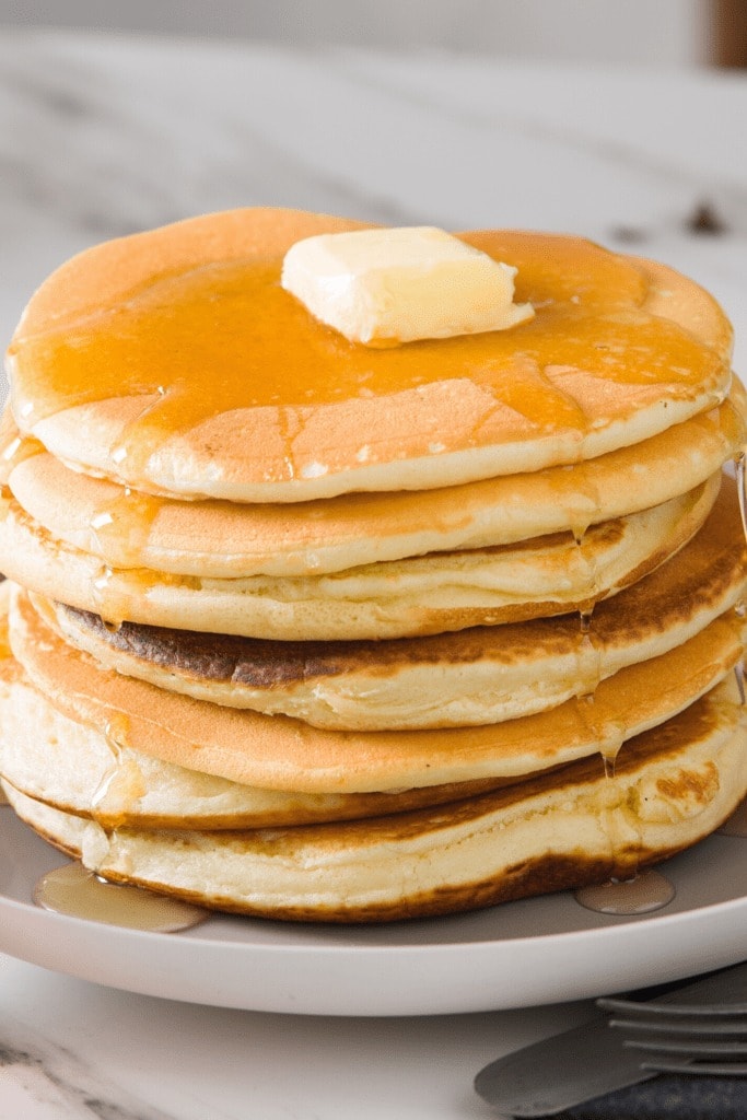 Stack of pancakes on a plate topped with slice of butter pancake syrup