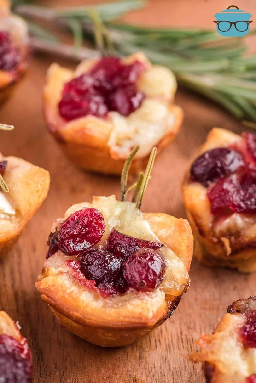 Baked brie bites with cranberry arranged on top of a wooden table. 