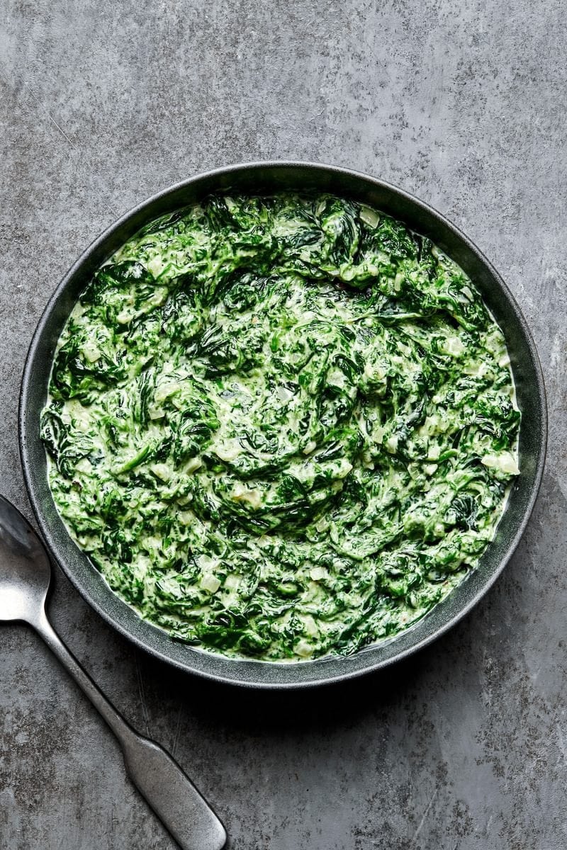 Black bowl of creamed spinach. 