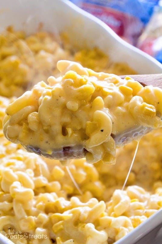 Wooden spoon scooping creamy corn macaroni and cheese from a casserole.