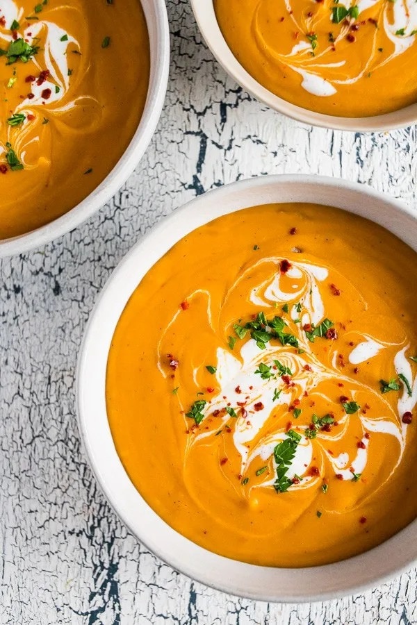 Bowl of creamy red lentil carrot soup with cream on top. 