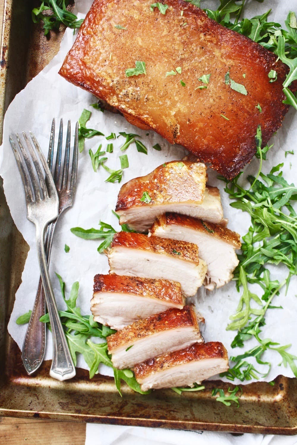 Crispy Instant Pot Pork Belly Whole and Slice on a tray with parchment paper garnished with arugula