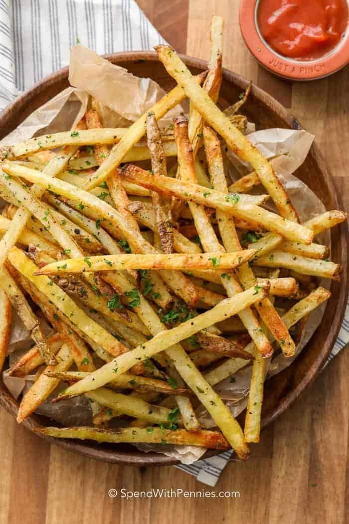 Wooden plate filled with crispy oven bake French fries seasoned with herbs with catsup dip on side. 