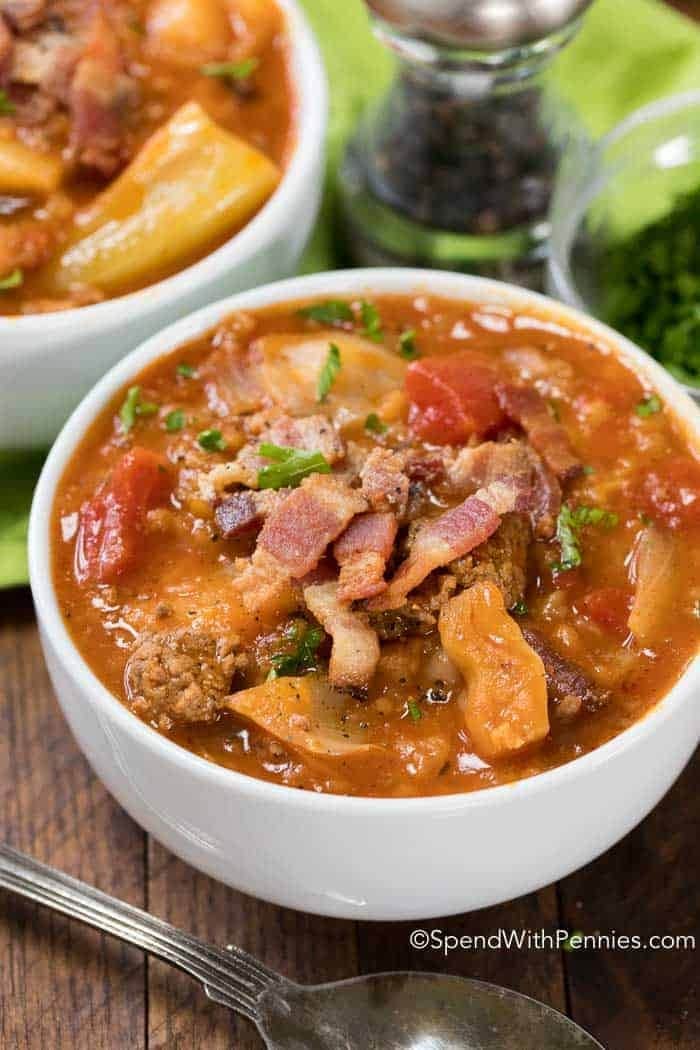 Cabbage roll soup served in bowls topped with bacons strips and chopped leaves. 