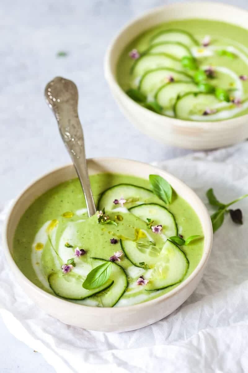 Bowls of homemade Cucumber Gazpacho with cucumber, spring onions, coconut yogurt, basil, parsley and mint leaves
