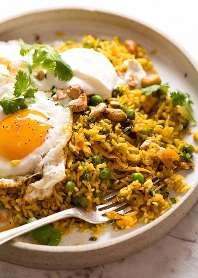Curried rice in a plate  with peas, nuts, meat and fried egg. 
