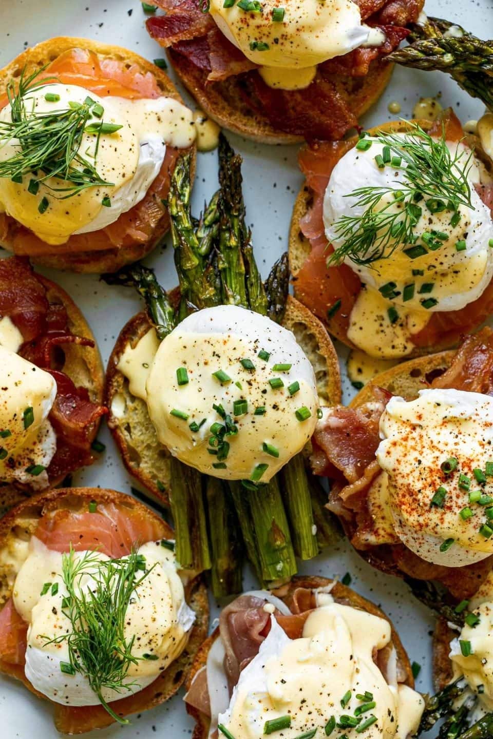 Eggs Benedict topped on toasted bread layered with bacon, asparagus and samon. 