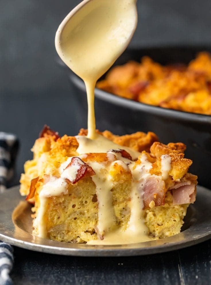 A slice of eggs benedict casserole made with english muffins, filled with ham, and topped off with a simple eggs benedict sauce served on a steel plate.