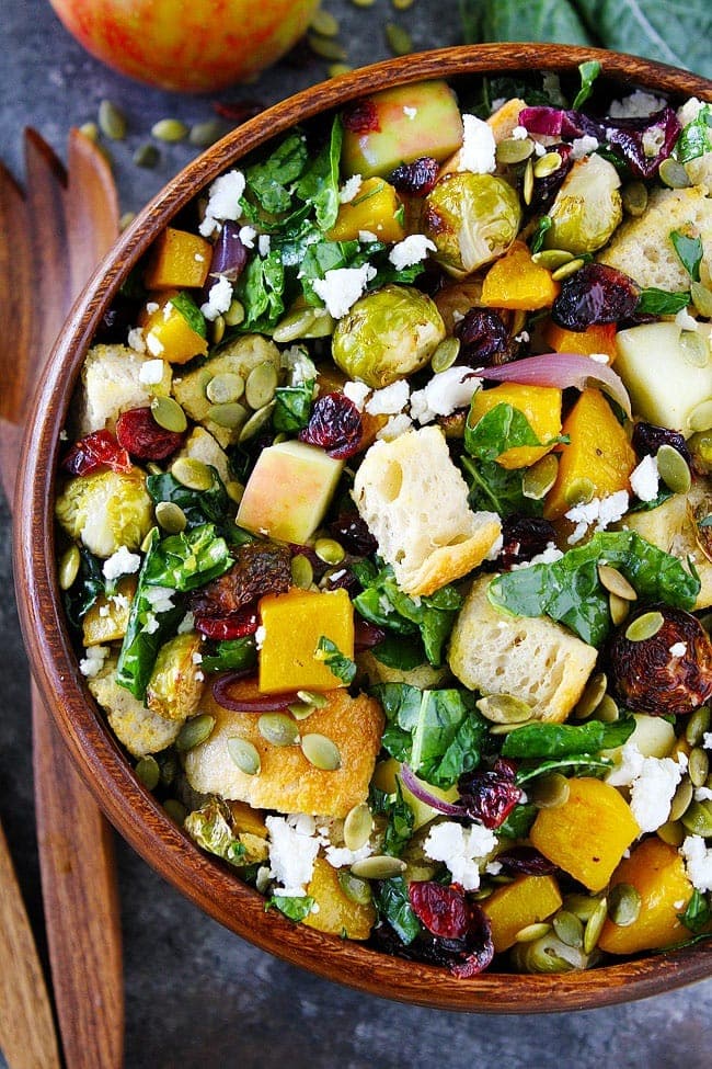 Fall panzanella salad in a wooden bowl with butternut squash, Brussels sprouts, apple, dried cranberries, pepitas, goat cheese, and kale.
