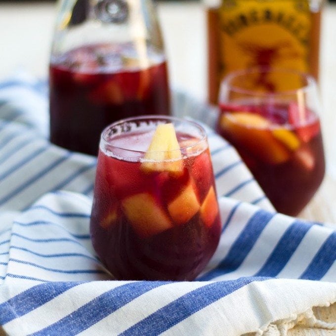Glasses of fireball sangria filled with fruit and a bottle of liquor in the background. 