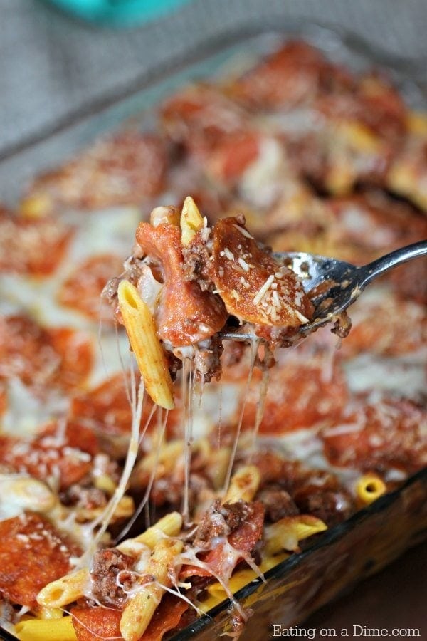 Spoon scooping cheesy pizza casserole form a glass dish. 