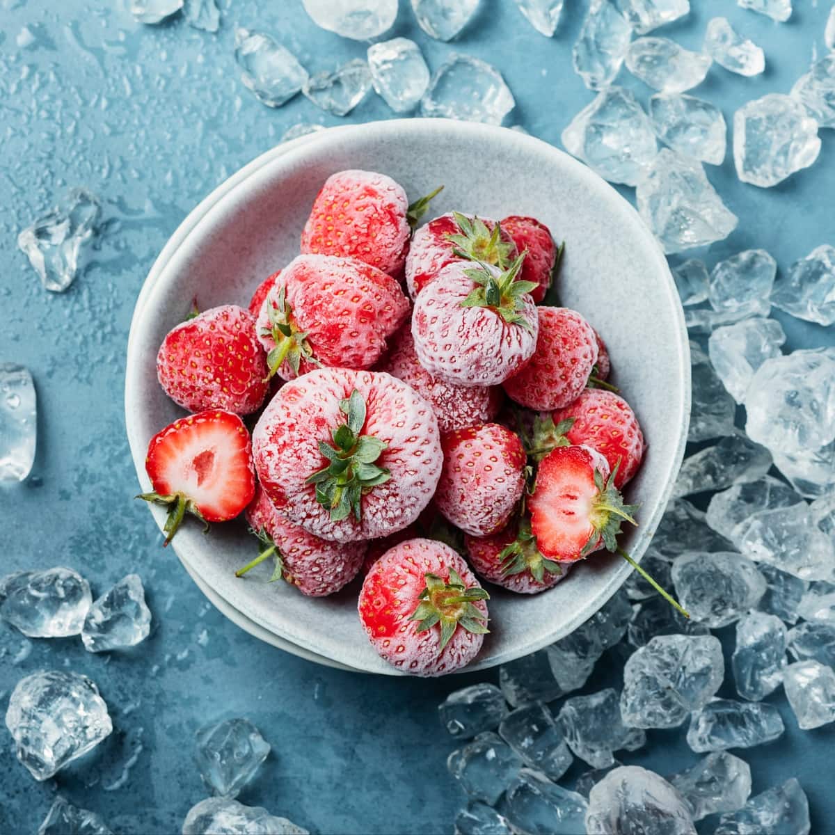 Bowl of  Whole and Sliced Frozen Strawberries on a Table, Surrounded By Chunks of Ice