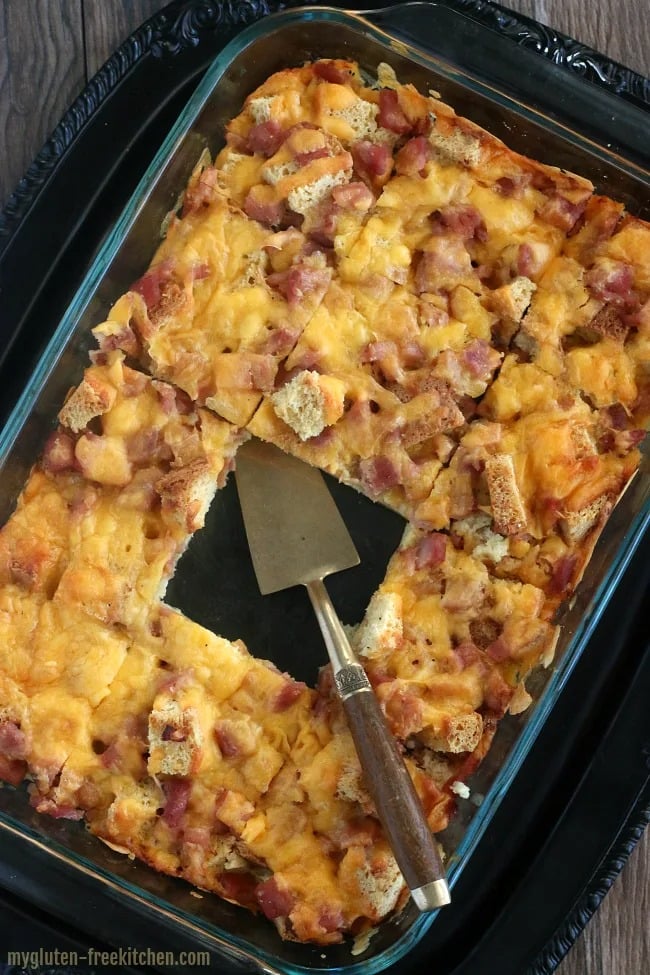 Sliced  Gluten-free overnight holiday breakfast casserole on a glass dish made with bread cubes and cheese. 