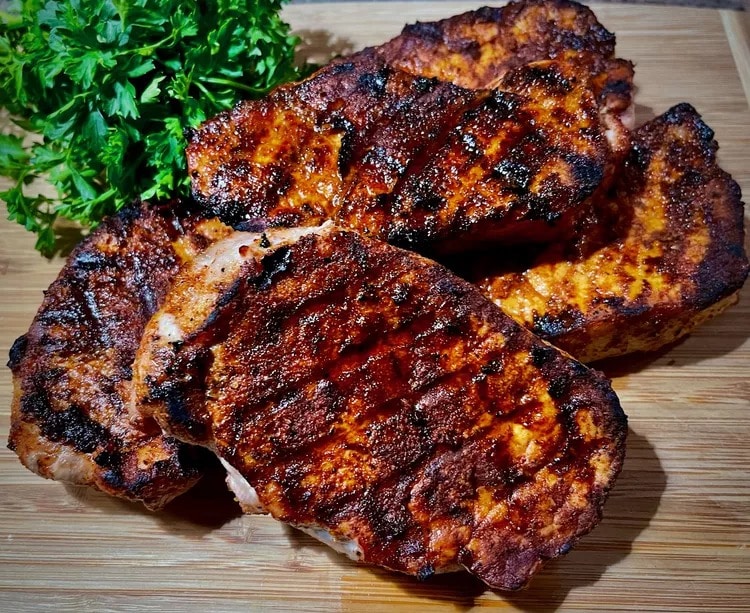 Grilled pork chops seasoned with smoked paprika rub on a wooden board. 
