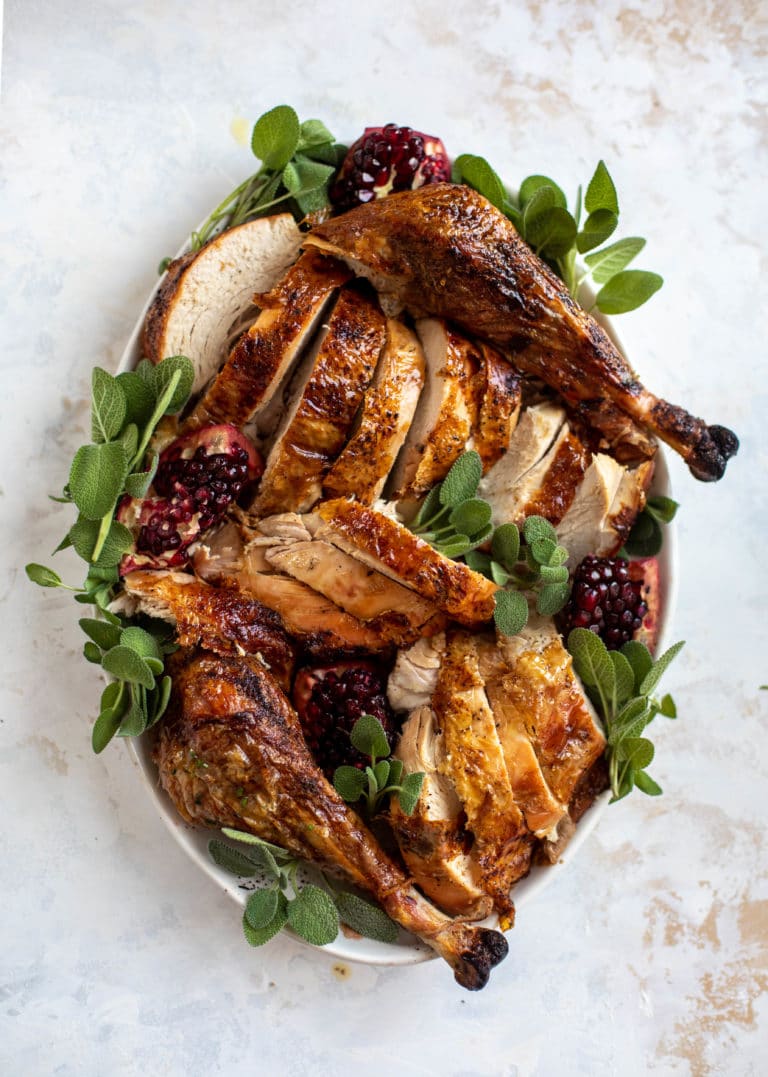 Chopped whole grilled turkey on an oval plate garnish with sage leaves and pomegranate