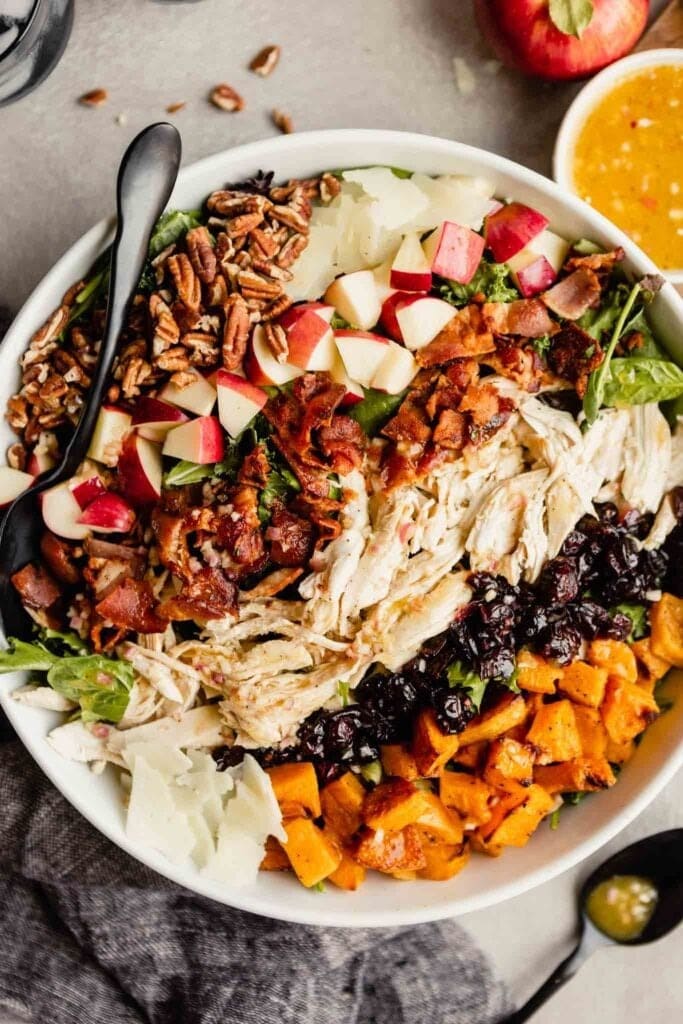 Bowl of turkey cobb salad  made with pecan nuts, apple slices, bacon, cranberries and squash. 
