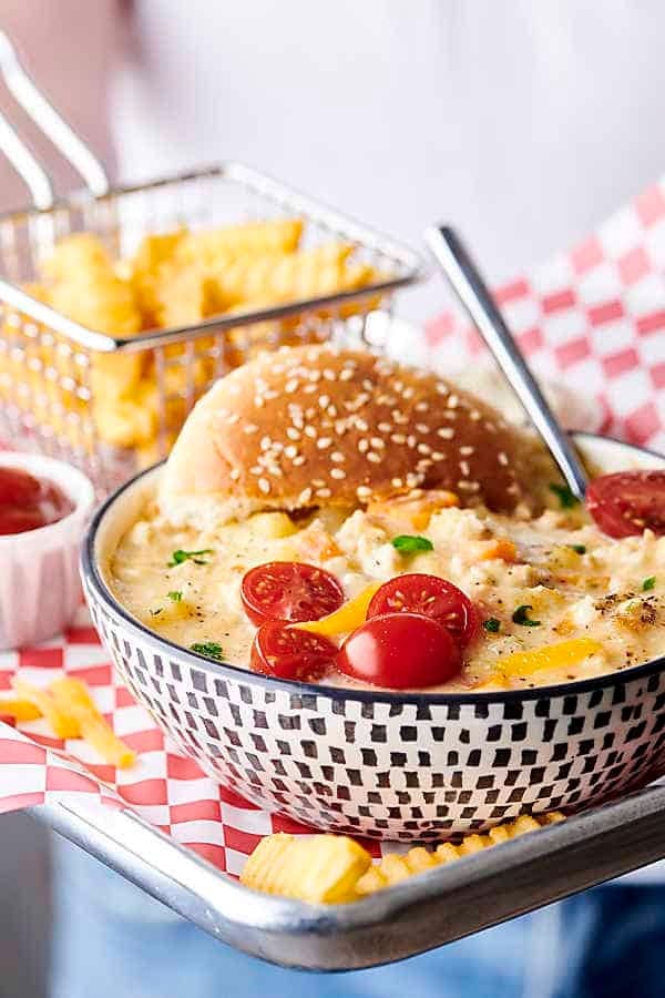 Cheeseburger soup loaded with turkey, potato, cauliflower, onion, carrot, and celery in a bowl served with burger buns. 