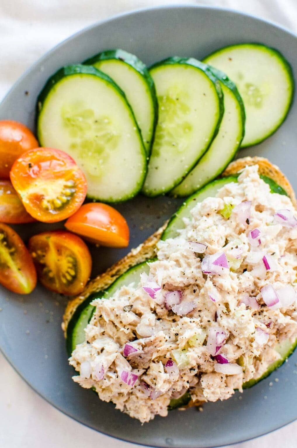 Healthy tuna salad on top of tasted brioche served with tomatoes and sliced cucumber. 