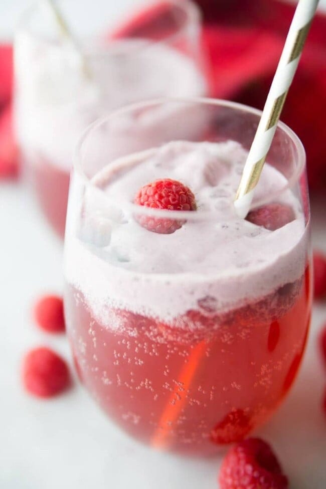 A glass of foamy cranberry raspberry holiday punch garnished with fresh cranberries. 