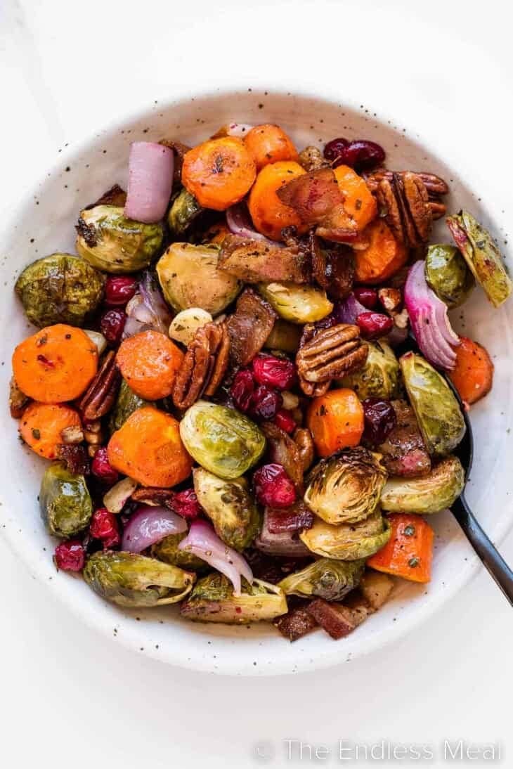 Roasted vegetables with onions, carrots, sprouts and cranberries on a bowl with spoon. 