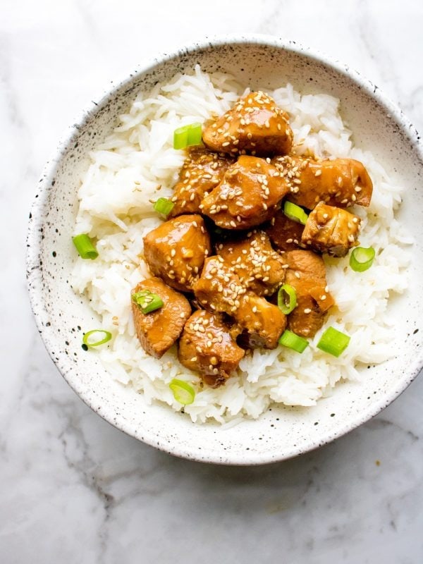 Hone sesame chicken served on top of white rice in a bowl. 
