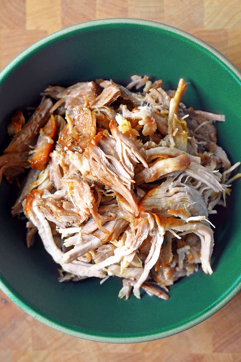 A bowl of shredded kalua pork on a wooden table, ready to be savored