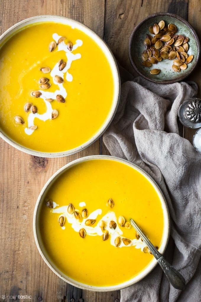 Two bowls of pumpkin soup garnished with pumpkin seeds. 