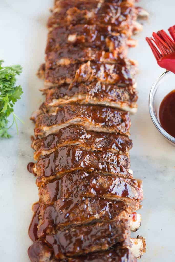 Ribs with savory sauce and aromatic herbs displayed on a wooden cutting board