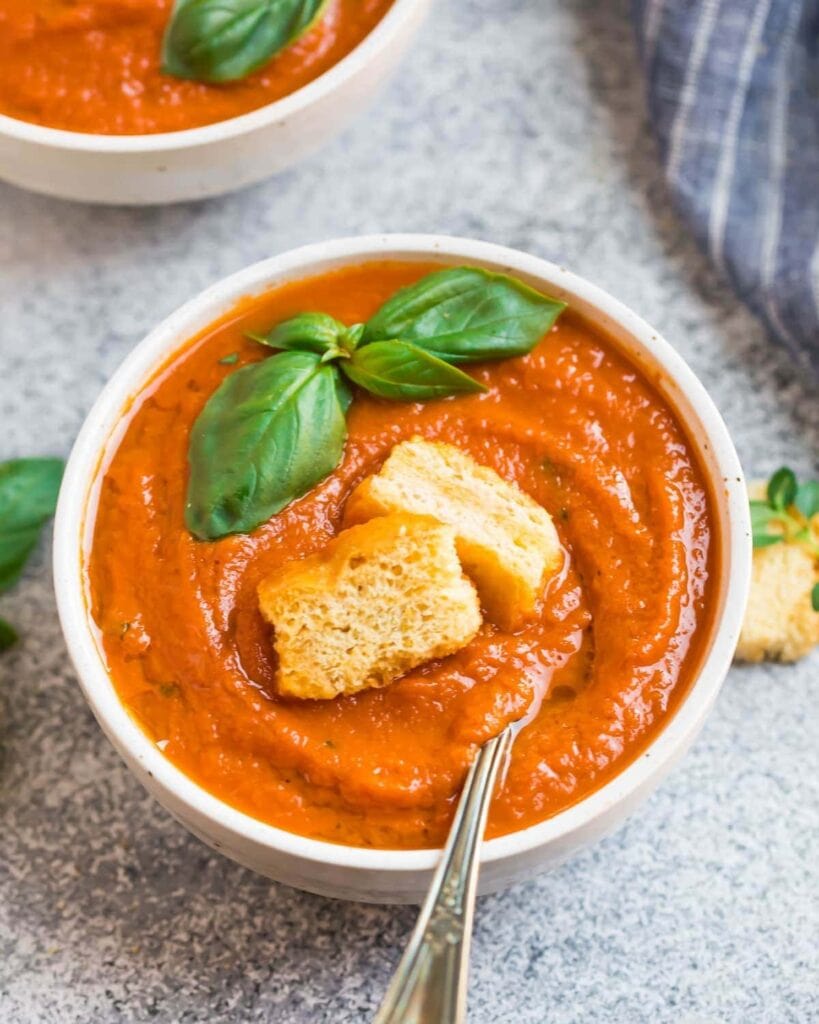 Bowl of tomato soup topped with croutons and fresh basil leaves. 